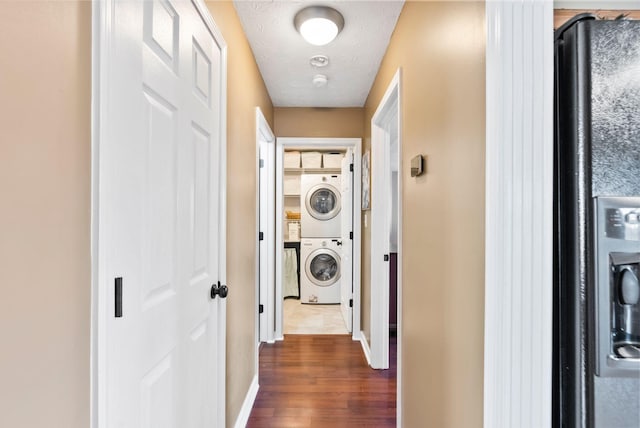 hall featuring stacked washer / dryer, dark wood-style flooring, a textured ceiling, and baseboards