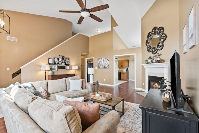 living room with high vaulted ceiling, a fireplace, visible vents, baseboards, and dark wood-style floors