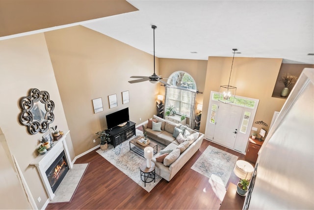 living room with baseboards, a tiled fireplace, ceiling fan, dark wood-style flooring, and high vaulted ceiling