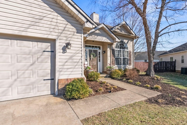 doorway to property with brick siding, a chimney, an attached garage, central AC unit, and fence