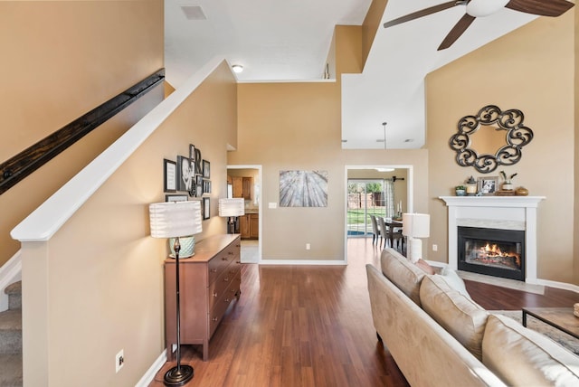 living room featuring ceiling fan, dark wood-type flooring, a high ceiling, baseboards, and stairs