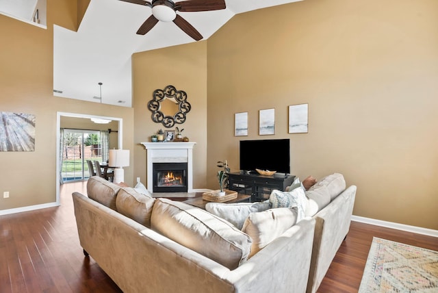 living room featuring baseboards, high vaulted ceiling, dark wood-type flooring, and a glass covered fireplace