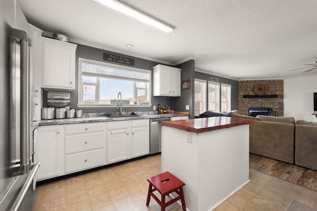 kitchen with open floor plan, stainless steel appliances, a fireplace, wooden counters, and a sink