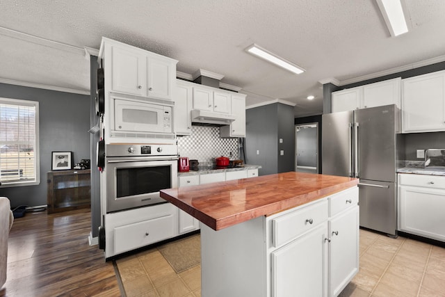 kitchen featuring wood counters, appliances with stainless steel finishes, a center island, crown molding, and under cabinet range hood