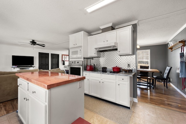 kitchen with white microwave, oven, under cabinet range hood, butcher block countertops, and white cabinetry