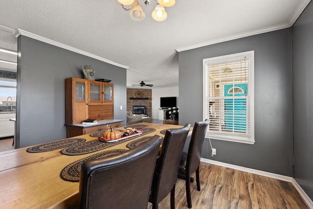 dining space featuring ornamental molding, a brick fireplace, a textured ceiling, wood finished floors, and baseboards