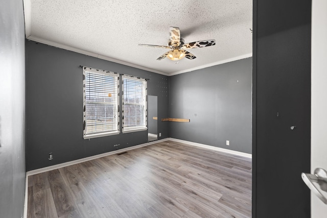 empty room with ornamental molding, a textured ceiling, and wood finished floors