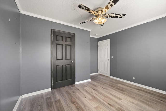 empty room with a textured ceiling, ornamental molding, wood finished floors, and baseboards