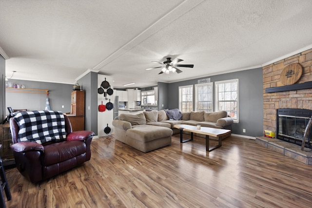 living room with crown molding, a fireplace, a textured ceiling, wood finished floors, and baseboards