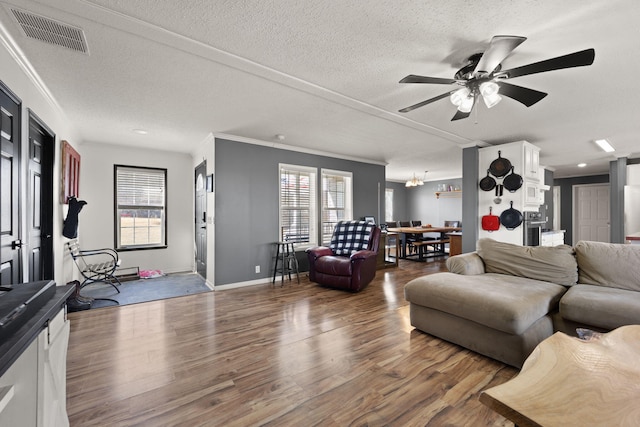 living area with ornamental molding, visible vents, and wood finished floors