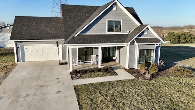 view of front of property with driveway, roof with shingles, an attached garage, covered porch, and a front yard