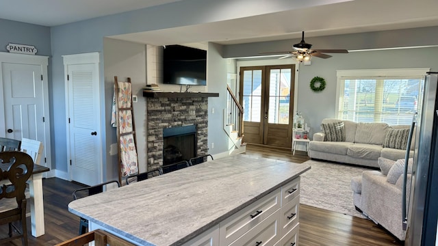 living area with a stone fireplace, dark wood-style flooring, a ceiling fan, baseboards, and stairway