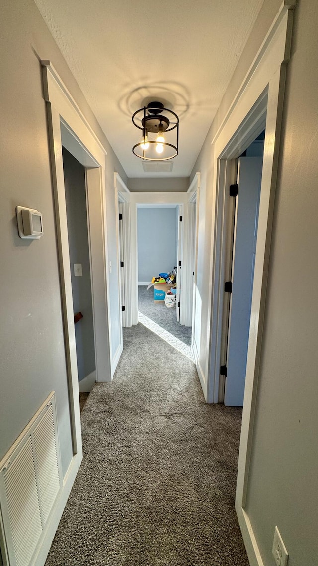 corridor featuring dark carpet, visible vents, and baseboards