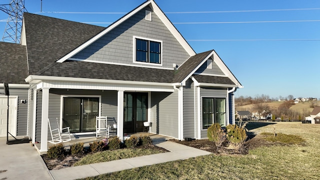 view of front of property with covered porch, roof with shingles, and a front yard