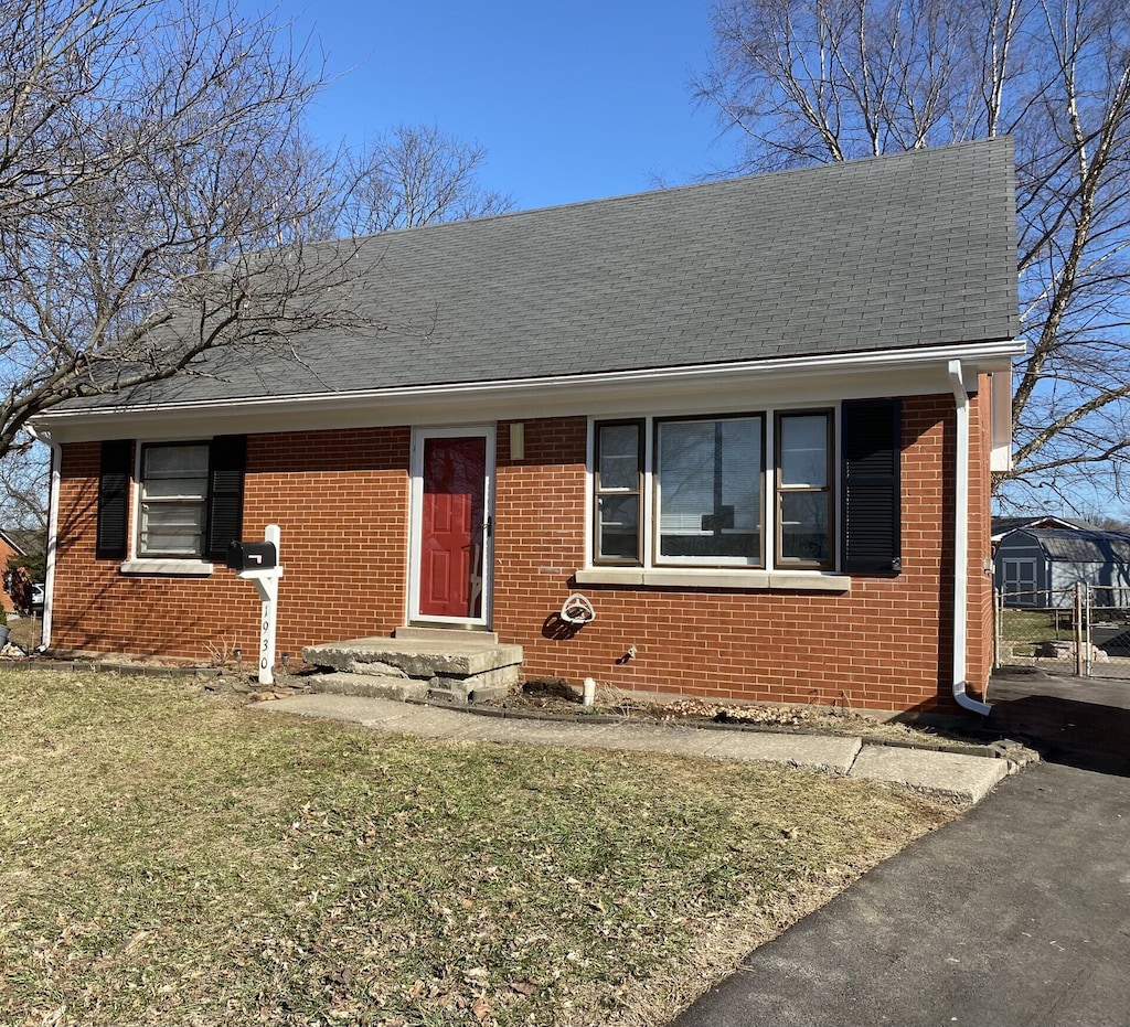 view of front facade with roof with shingles, a front lawn, and brick siding