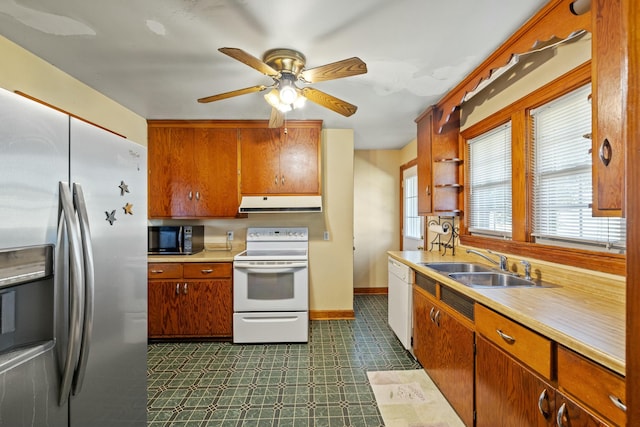 kitchen featuring light countertops, brown cabinetry, a sink, white appliances, and under cabinet range hood