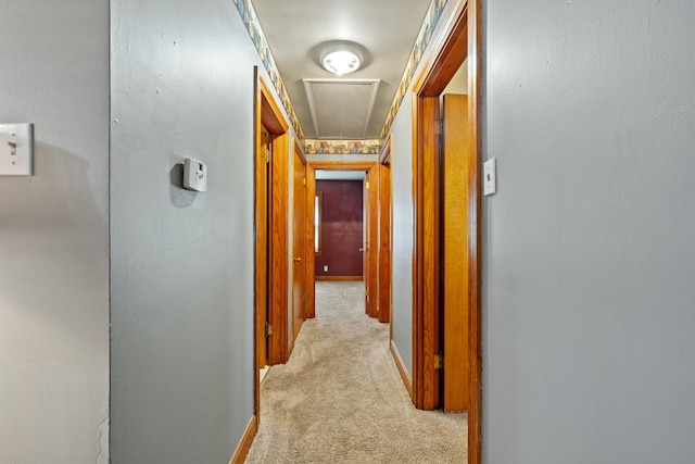 corridor with light carpet, attic access, and baseboards