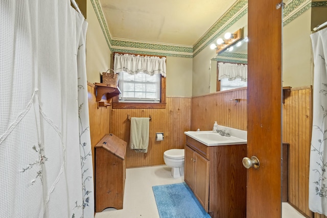 full bath featuring toilet, wooden walls, a wainscoted wall, vanity, and crown molding