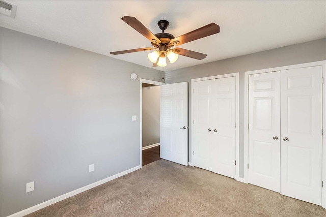 unfurnished bedroom with ceiling fan, light colored carpet, visible vents, baseboards, and multiple closets