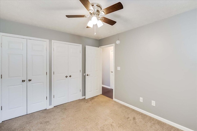 unfurnished bedroom featuring baseboards, light colored carpet, ceiling fan, a textured ceiling, and two closets