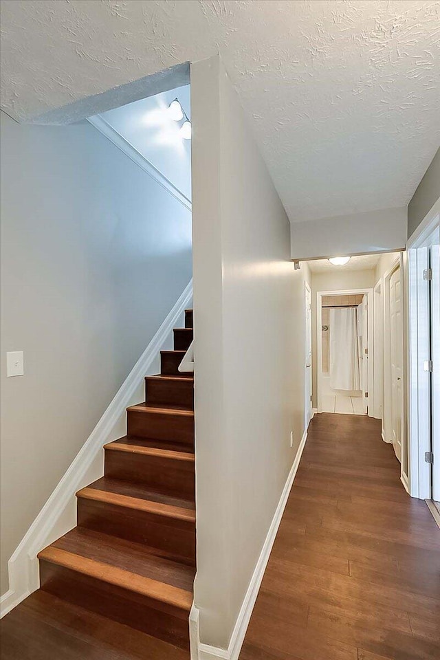 hallway featuring baseboards, a textured ceiling, stairway, and dark wood-type flooring