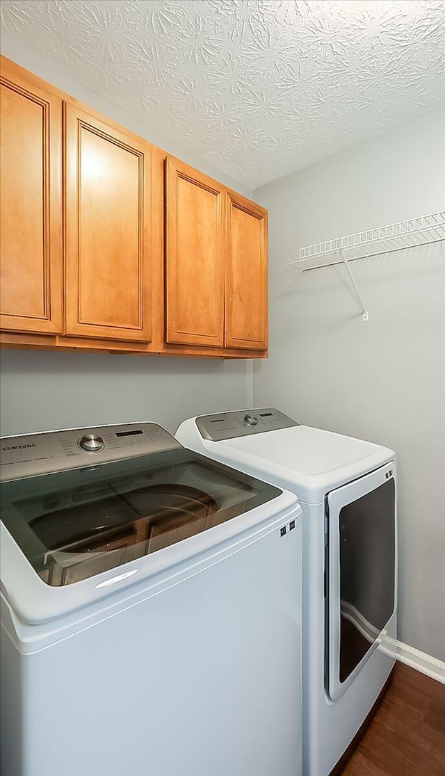 laundry area with dark wood-style floors, cabinet space, a textured ceiling, separate washer and dryer, and baseboards