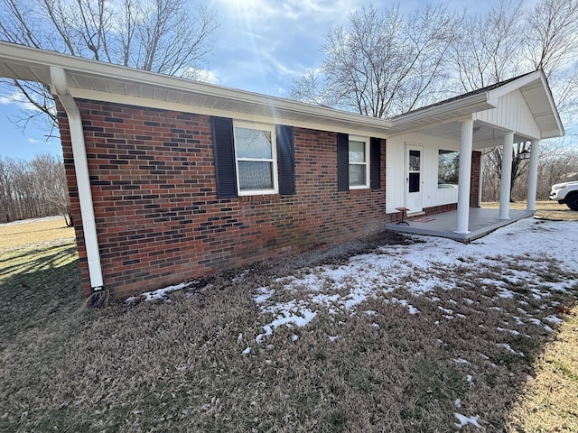 snow covered property with covered porch and brick siding