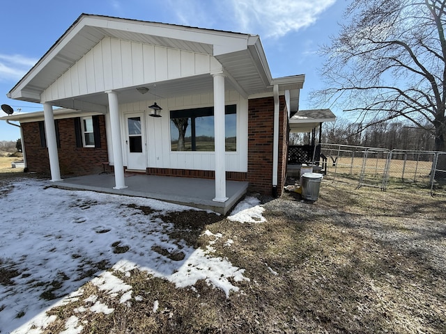 snow covered rear of property with a porch, brick siding, and fence