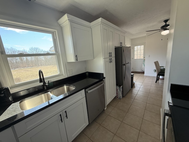 kitchen featuring light tile patterned floors, dark countertops, appliances with stainless steel finishes, white cabinets, and a sink