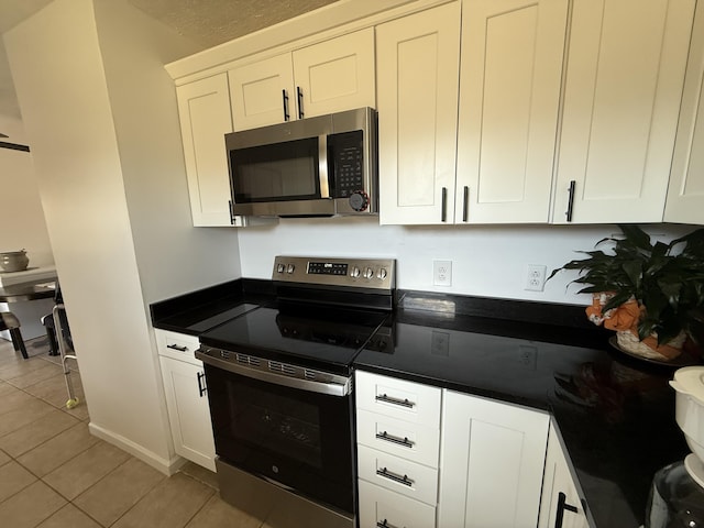 kitchen with dark countertops, white cabinetry, stainless steel appliances, and light tile patterned flooring