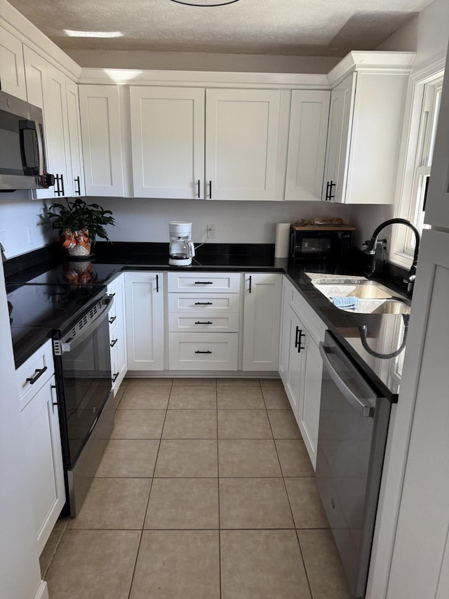 kitchen with stainless steel appliances, dark countertops, white cabinetry, and a sink