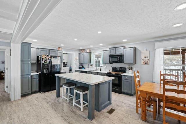 kitchen featuring a breakfast bar, a center island, gray cabinets, black appliances, and a sink