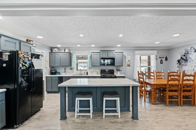 kitchen featuring a breakfast bar area, a sink, a kitchen island, light stone countertops, and black appliances