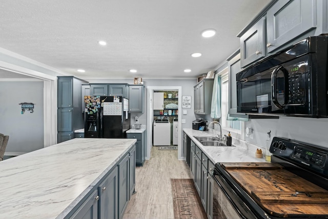 kitchen featuring recessed lighting, a sink, washer and dryer, light wood-style floors, and black appliances