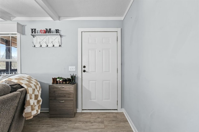 doorway to outside featuring a textured ceiling, light wood finished floors, beamed ceiling, and baseboards