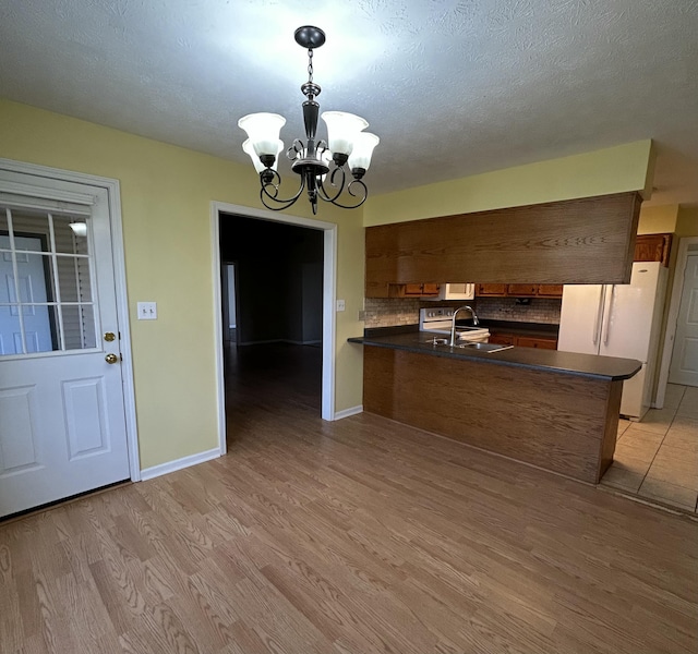 kitchen featuring dark countertops, light wood-style flooring, a sink, white appliances, and a peninsula