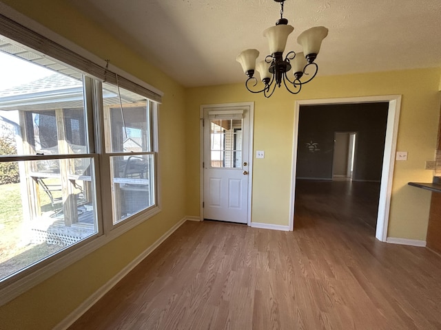 entryway with baseboards, wood finished floors, a wealth of natural light, and an inviting chandelier