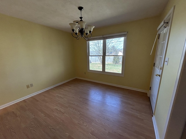 unfurnished dining area featuring baseboards, a textured ceiling, a chandelier, and wood finished floors