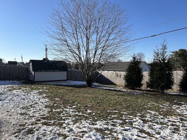 yard layered in snow featuring a storage unit, an outdoor structure, and a fenced backyard