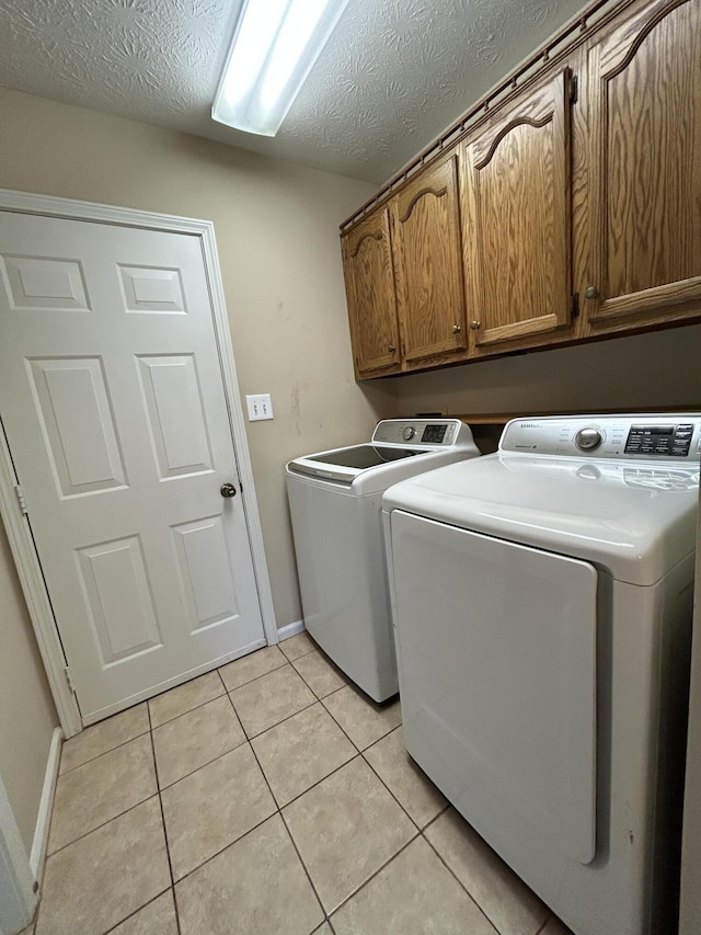 clothes washing area featuring cabinet space, light tile patterned floors, baseboards, a textured ceiling, and separate washer and dryer