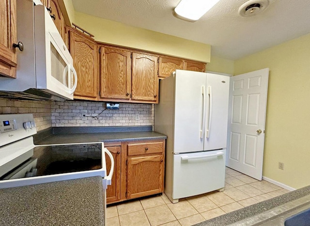 kitchen featuring light tile patterned flooring, white appliances, decorative backsplash, brown cabinetry, and dark countertops