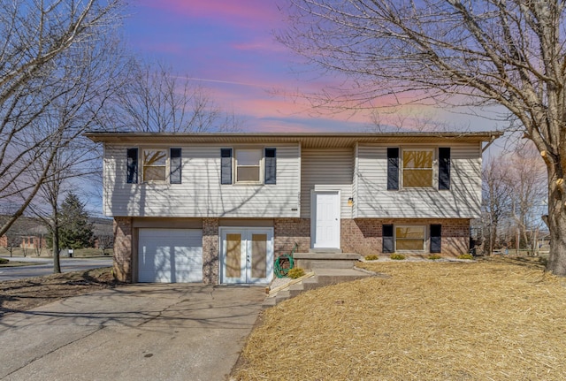 raised ranch with an attached garage, aphalt driveway, and brick siding