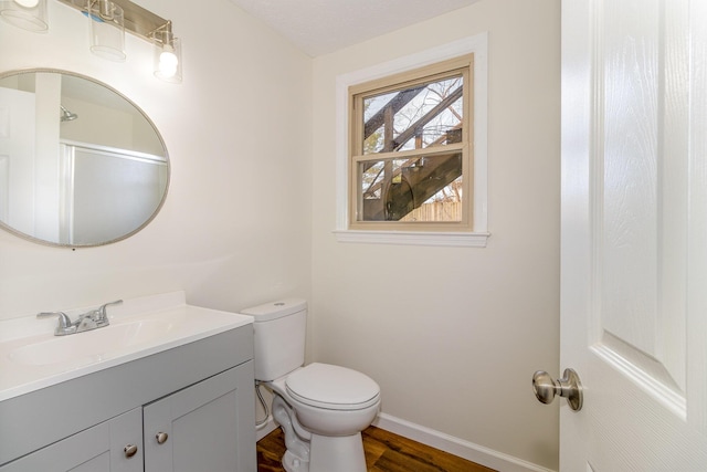 bathroom featuring toilet, baseboards, wood finished floors, and vanity