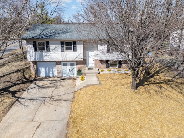 split foyer home with brick siding, roof with shingles, a front yard, a garage, and driveway