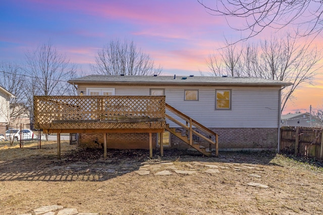 back of property at dusk with stairs, brick siding, fence, and a wooden deck