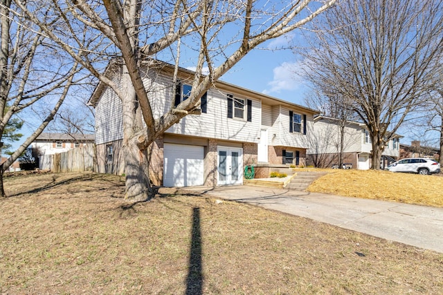 bi-level home with driveway, brick siding, an attached garage, fence, and a front yard