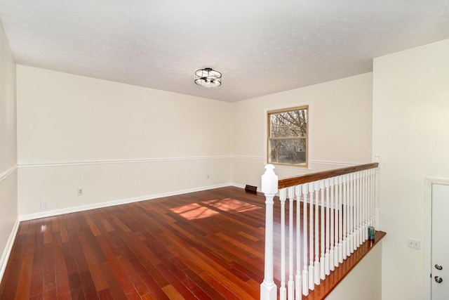 unfurnished room with a textured ceiling, baseboards, and wood finished floors