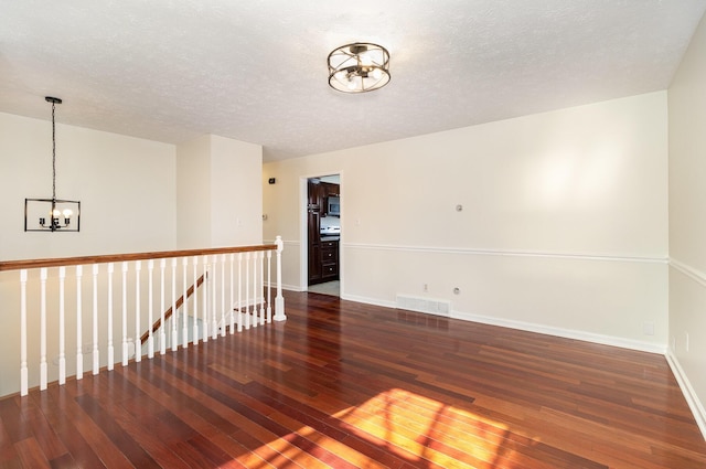 empty room with wood-type flooring, visible vents, a textured ceiling, a chandelier, and baseboards