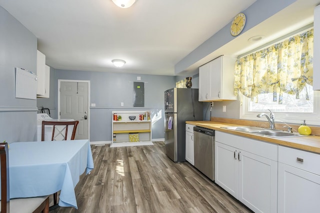 kitchen with stainless steel appliances, a sink, wood finished floors, wood counters, and white cabinets