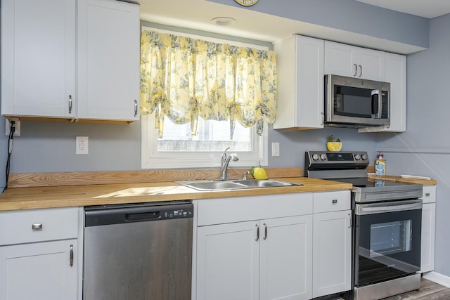 kitchen featuring white cabinets, butcher block countertops, stainless steel appliances, and a sink